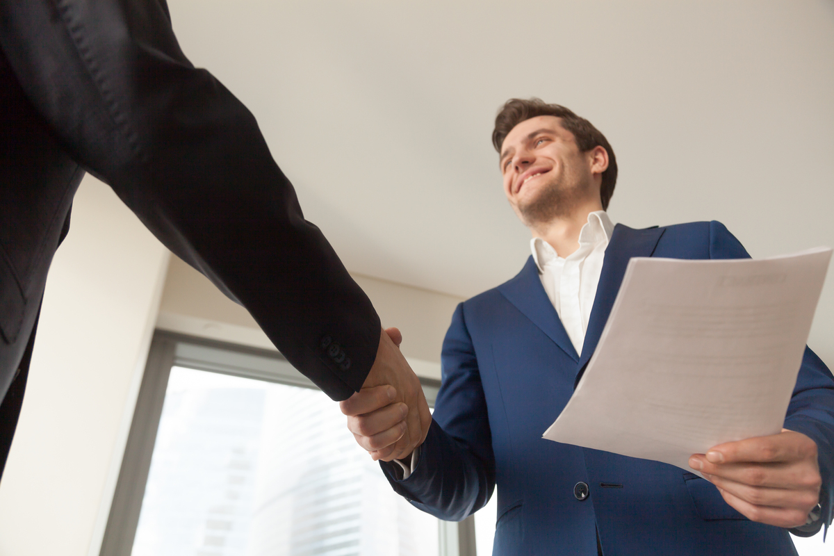 Satisfied businessman with business documents shaking hand to partner, making deal after reviewing terms of contract, offering profitable project to investor, happy of partnership, welcoming client